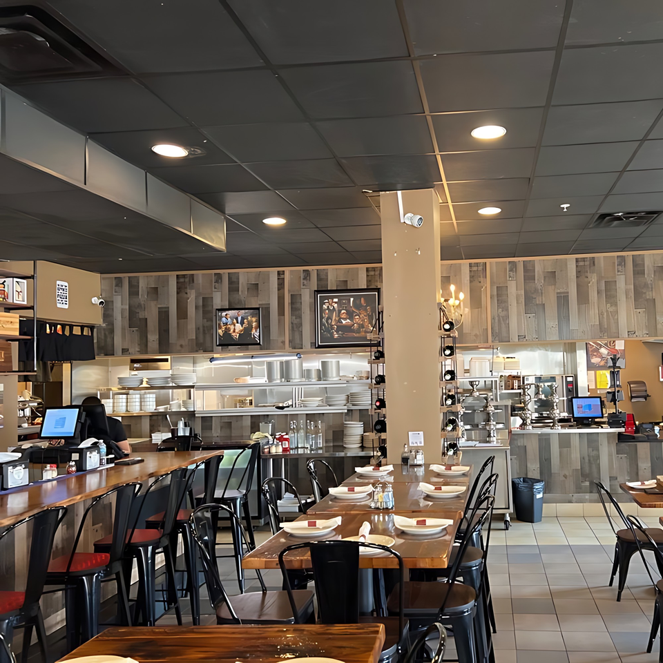 Interior of Cucina Pizza & Bar, showing dining tables, bar seating, and an open kitchen area.