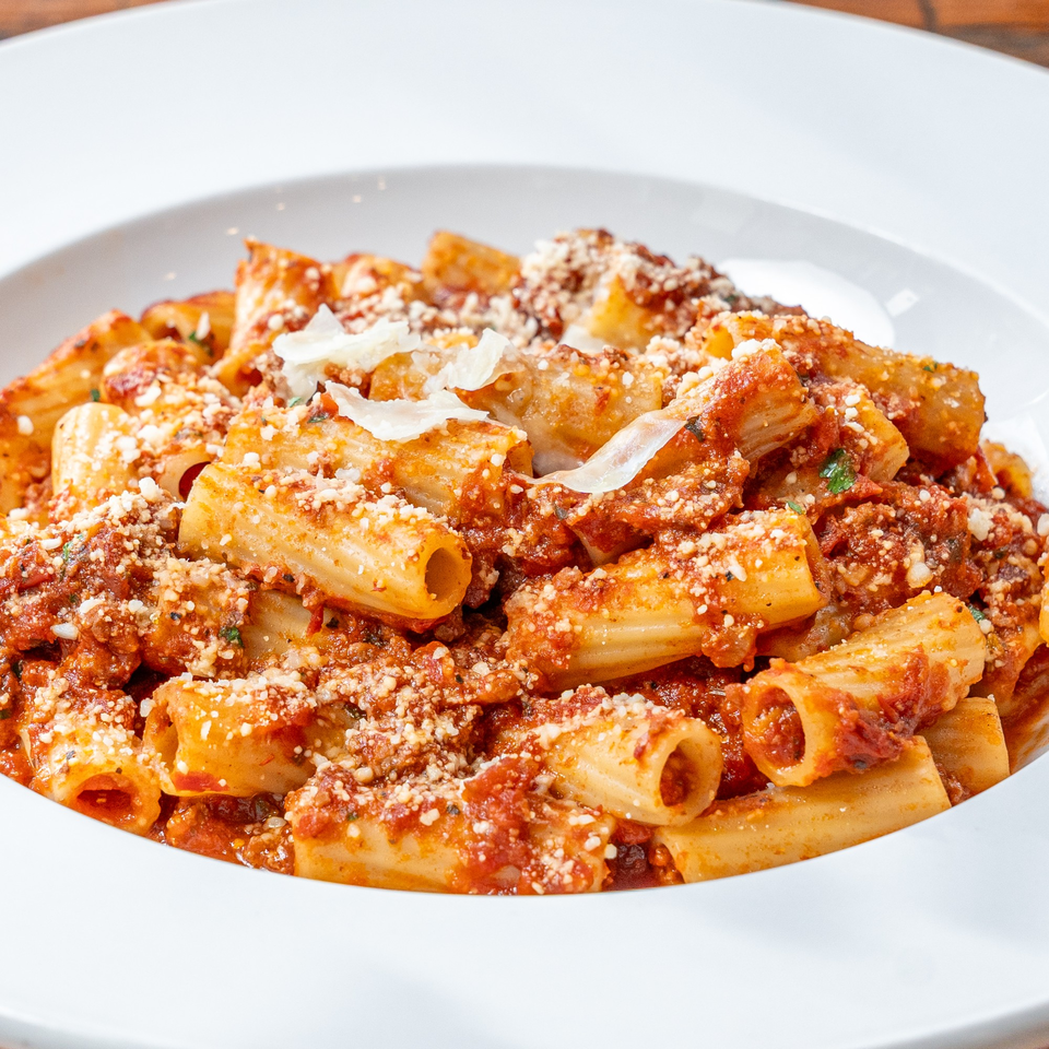 Rigatoni pasta with rich red sauce, grated cheese, and fresh herbs in a white bowl.