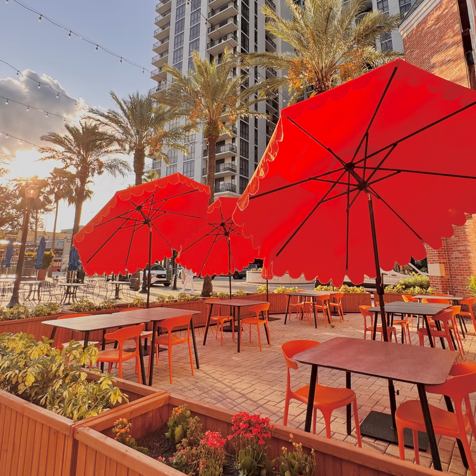 Cucina Pizza & Bar's outdoor patio with red umbrellas, orange chairs, and palm trees.
