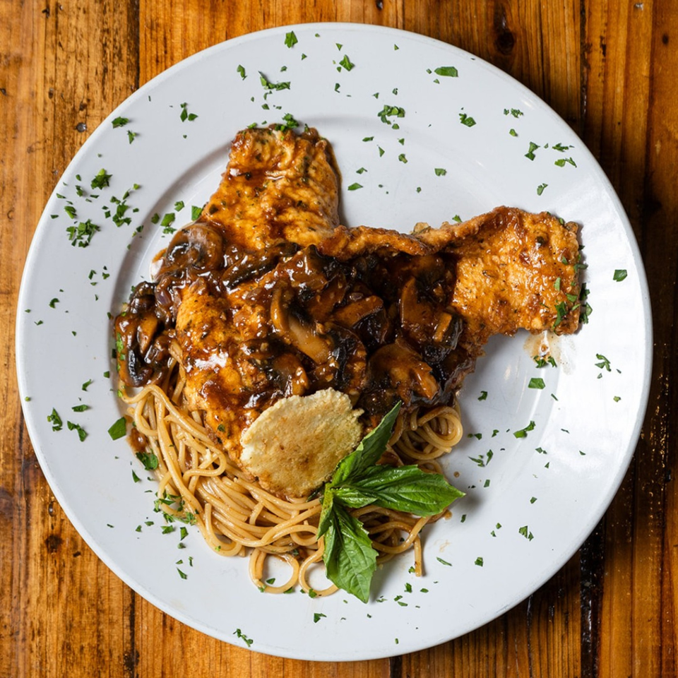 Chicken Marsala with mushrooms and spaghetti, garnished with basil and a parmesan crisp.